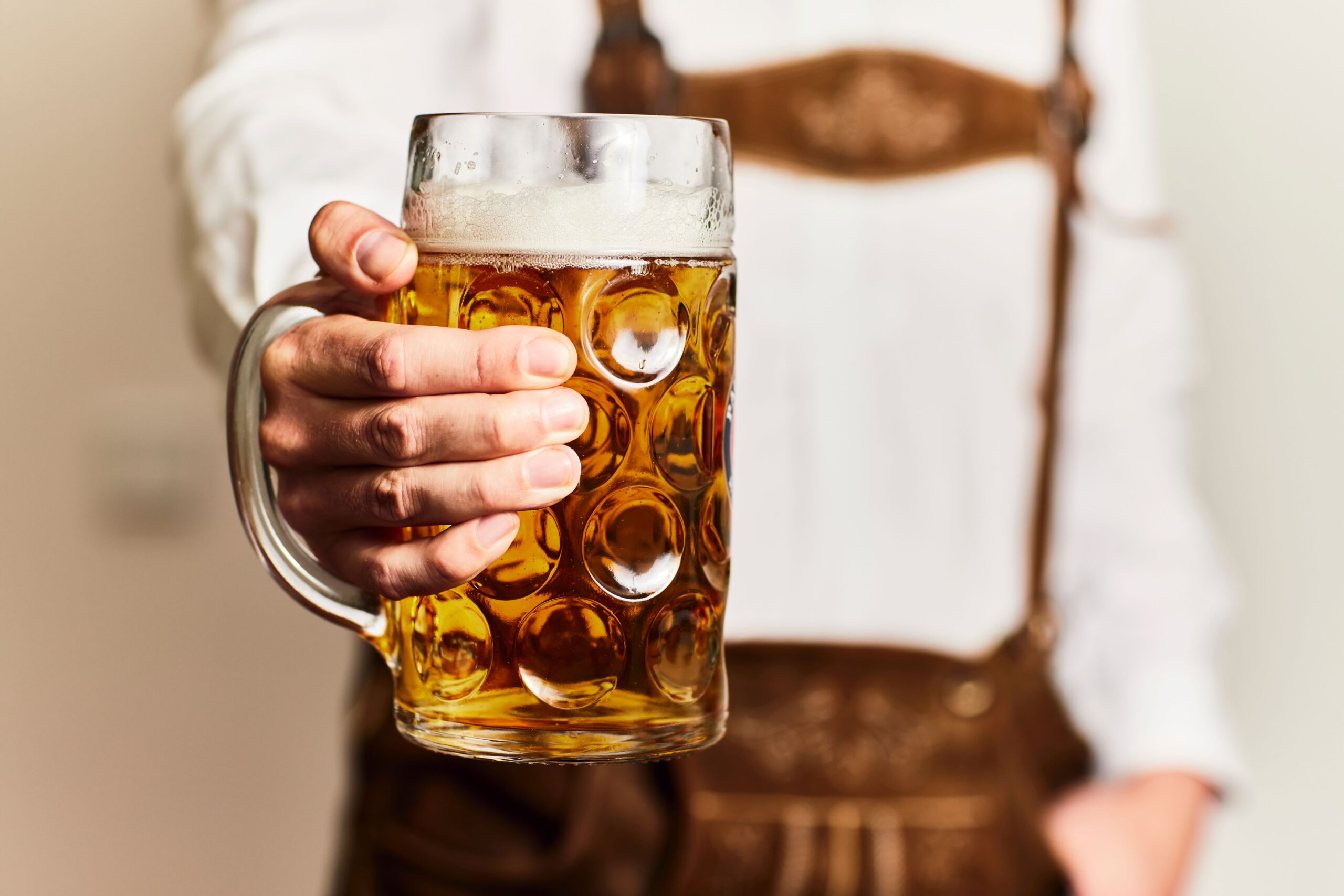 Ein Mann in Lederhosen hält ein Bier in der Hand